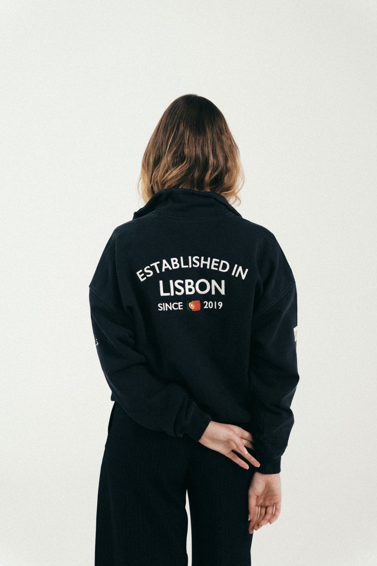 Esenzia Worldwide · lookbook · half-zip negro, Lisbon a la espalda